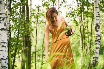 A young woman mother straightens her loose green dress standing among the green meadows and birches. The concept of pregnancy and unity with nature
