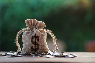 money bag on wood with coins stack in morning light. concept saving