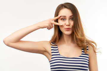 Fototapeta premium A pretty cheerful girl in a striped t-shirt with long curly hair shows a peace sign with her hand. Isolated portrait on white background