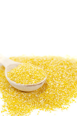 Yellow corn grits are in a wooden spoon on a white background