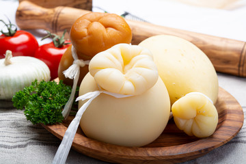 Italian provolone or provola caciocavallo hard and smoked cheeses in teardrop form served on olive tree board close up