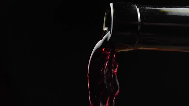 Wine. Red wine pouring from neck of bottle in wine glass over dark background. Rose wine pouring from the bottle. Slow motion