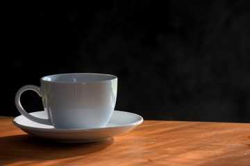 Coffee in a white glass, wooden floor and black background with morning light. 