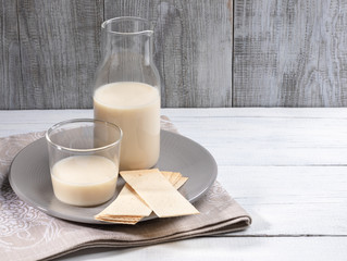 Dairy free oat milk in glass bottle and glass on white table on grey wooden background. 