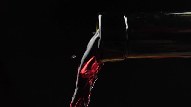 Wine. Red wine pouring from neck of bottle in wine glass over dark background. Rose wine pouring from the bottle. Slow motion