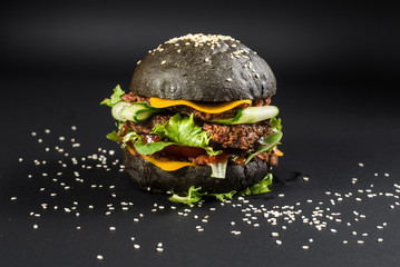 Tasty craft burger with black bun on the black background
