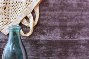 Glass milk bottle and knitted food bag on grey background. Reusable packaging. The concept of environmental protection.