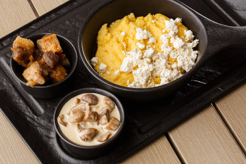 Typical Ukrainian dish polenta - Banosh with cheese and lard. Ukrainian cuisine. maize porridge with bacon, cracklings and cheese Corn porridge in plate on wooden background.