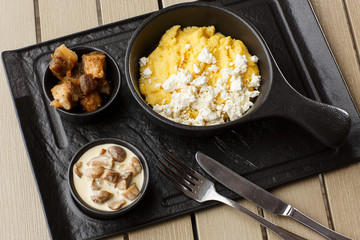 Typical Ukrainian dish polenta - Banosh with cheese and lard. Ukrainian cuisine. maize porridge with bacon, cracklings and cheese Corn porridge in plate on wooden background.