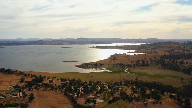Aerial, drone shot towards lake Huma, overlooking a small village and trees on the shore, on a sunny evening, at Hume Reservoir, between New South Wales and Victoria, in Australia