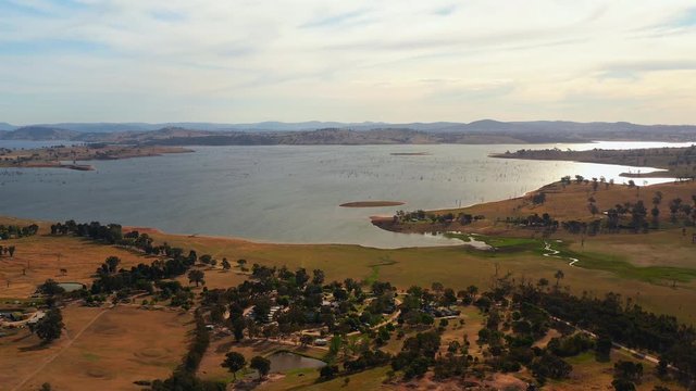 Aerial, tracking, drone shot overlooking lake Huma, a small village and trees on the shore, on a sunny evening, at Hume Reservoir, between New South Wales and Victoria, in Australia