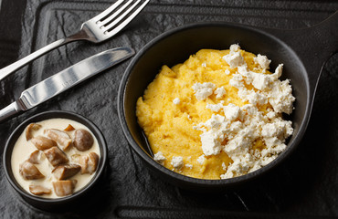 Typical Ukrainian dish polenta - Banosh with cheese and lard. Ukrainian cuisine. maize porridge with bacon, cracklings and cheese Corn porridge in plate on wooden background.