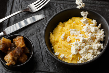 Typical Ukrainian dish polenta - Banosh with cheese and lard. Ukrainian cuisine. maize porridge with bacon, cracklings and cheese Corn porridge in plate on wooden background.