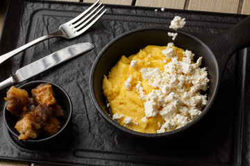 Typical Ukrainian dish polenta - Banosh with cheese and lard. Ukrainian cuisine. maize porridge with bacon, cracklings and cheese Corn porridge in plate on wooden background.