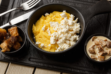 Typical Ukrainian dish polenta - Banosh with cheese and lard. Ukrainian cuisine. maize porridge with bacon, cracklings and cheese Corn porridge in plate on wooden background.