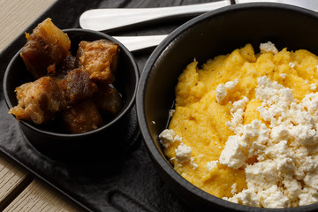 Typical Ukrainian dish polenta - Banosh with cheese and lard. Ukrainian cuisine. maize porridge with bacon, cracklings and cheese Corn porridge in plate on wooden background.