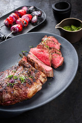 Barbecue dry aged wagyu tri tip steak sliced with hot sauce and tomato onion skewer as closeup on a modern design cast iron plate