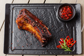 Grilled and barbecue hot pork ribs with hot chilli pepper and hot sauce on black stone background. Isolated. Dish for men. Spicy