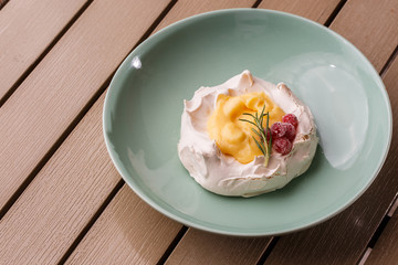Pavlova mini cake with custard cream and fresh summer berries on green plate on wooden background. Baked meringue cake.