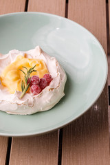 Pavlova mini cake with custard cream and fresh summer berries on green plate on wooden background. Baked meringue cake.