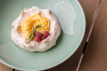 Pavlova mini cake with custard cream and fresh summer berries on green plate on wooden background. Baked meringue cake.