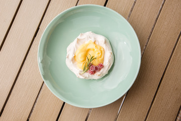 Pavlova mini cake with custard cream and fresh summer berries on green plate on wooden background. Baked meringue cake.