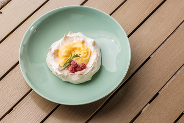 Pavlova mini cake with custard cream and fresh summer berries on green plate on wooden background. Baked meringue cake.