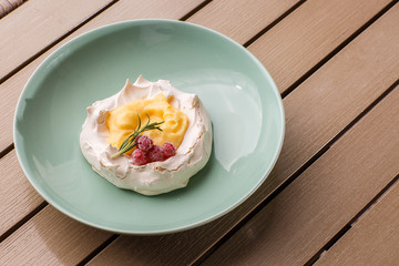Pavlova mini cake with custard cream and fresh summer berries on green plate on wooden background. Baked meringue cake.