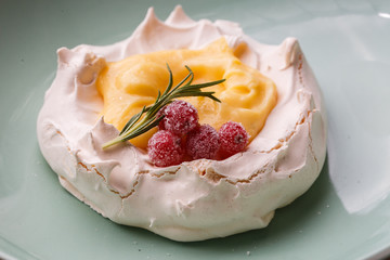 Pavlova mini cake with custard cream and fresh summer berries on green plate on wooden background. Baked meringue cake.