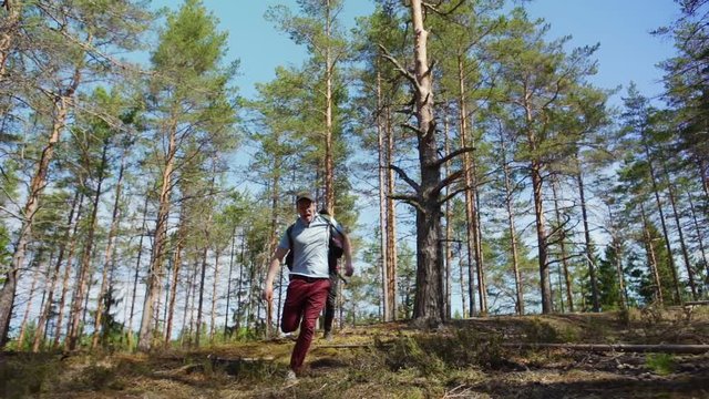 Two terribly scared young hikers running through forest in slow motion fleeing from somebody, throwing stick and screaming awfully, low angle view