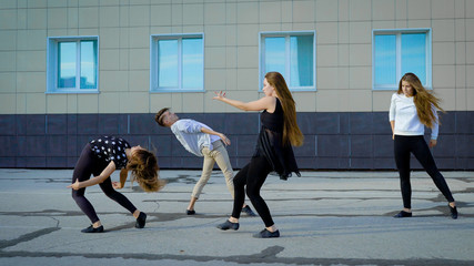 four contemporary dancers is rehearsing modern dance on a street in front of building in daytime