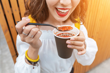 Woman eating street food vegan tomato soup from a paper takeaway cup. Modern fastfood concept