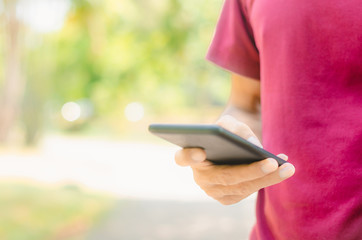 close up handsome man use hand typing mobile phones and touch screen working search with app devices in park with sunrise and green blur nature background.