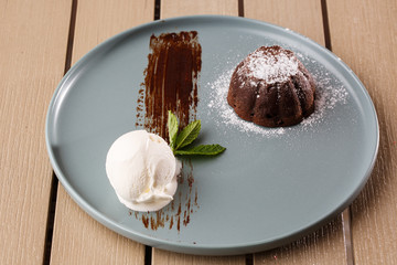 Delicious fresh fondant with hot chocolate and ice cream and mint served on plate. Lava cake recipe. Wooden background.