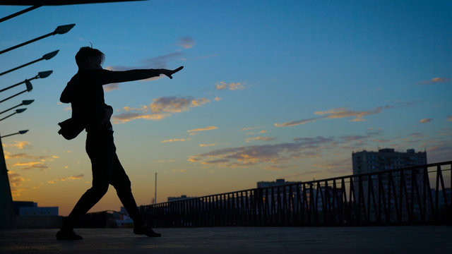 A man is dancing against a background of the evening sky. Dance in the style of Contemporary.