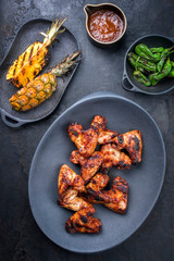 Exotically barbecue chicken wings with hot chili sauce, jalapeno and pineapple as top view on a cast iron plate