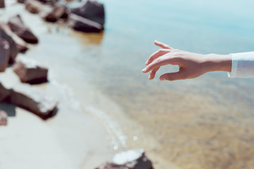 cropped view of woman hand on beach and river background