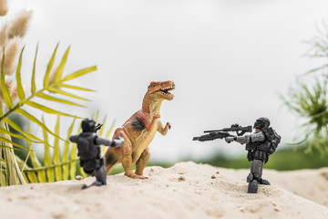 toy soldiers aiming with guns at toy dinosaur on sand hill