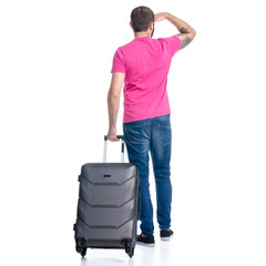 Man in jeans with travel suitcase standing looking away on white background isolation, back view