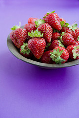 Fresh strawberries in a plate on a dark purple background.