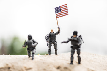 selective focus of toy soldier with weapon holding american flag on sand