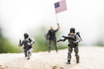 Selective focus of toy soldiers with weapon and American flag on sand