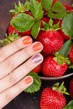 Hand with short manicured nails colored with red nail polish and strawberries