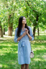 Fototapeta premium A girl of Asian appearance on a walk in a city park. Summer portrait of young Tatar on a background of green foliage