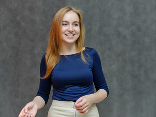 Concept portrait portrait of a beautiful smiling girl woman with red hair in a blue jacket. Something tells on a dark gray background. Shows emotions. Made in a studio.