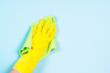 Hand in yellow gloves and microfiber rag cleaning blue background.