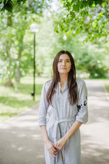 A girl of Asian appearance on a walk in a city park. Summer portrait of young Tatar on a background of green foliage
