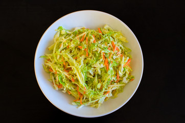 Homemade coleslaw salad in a white plate on a black background.