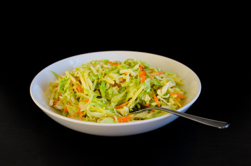 Homemade coleslaw salad in a white plate on a black background.