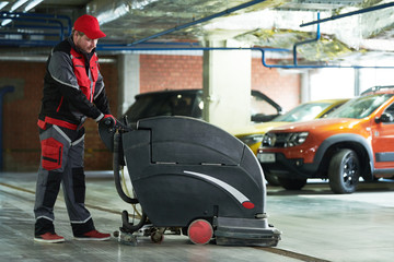 worker with machine cleaning floor in parking garage.